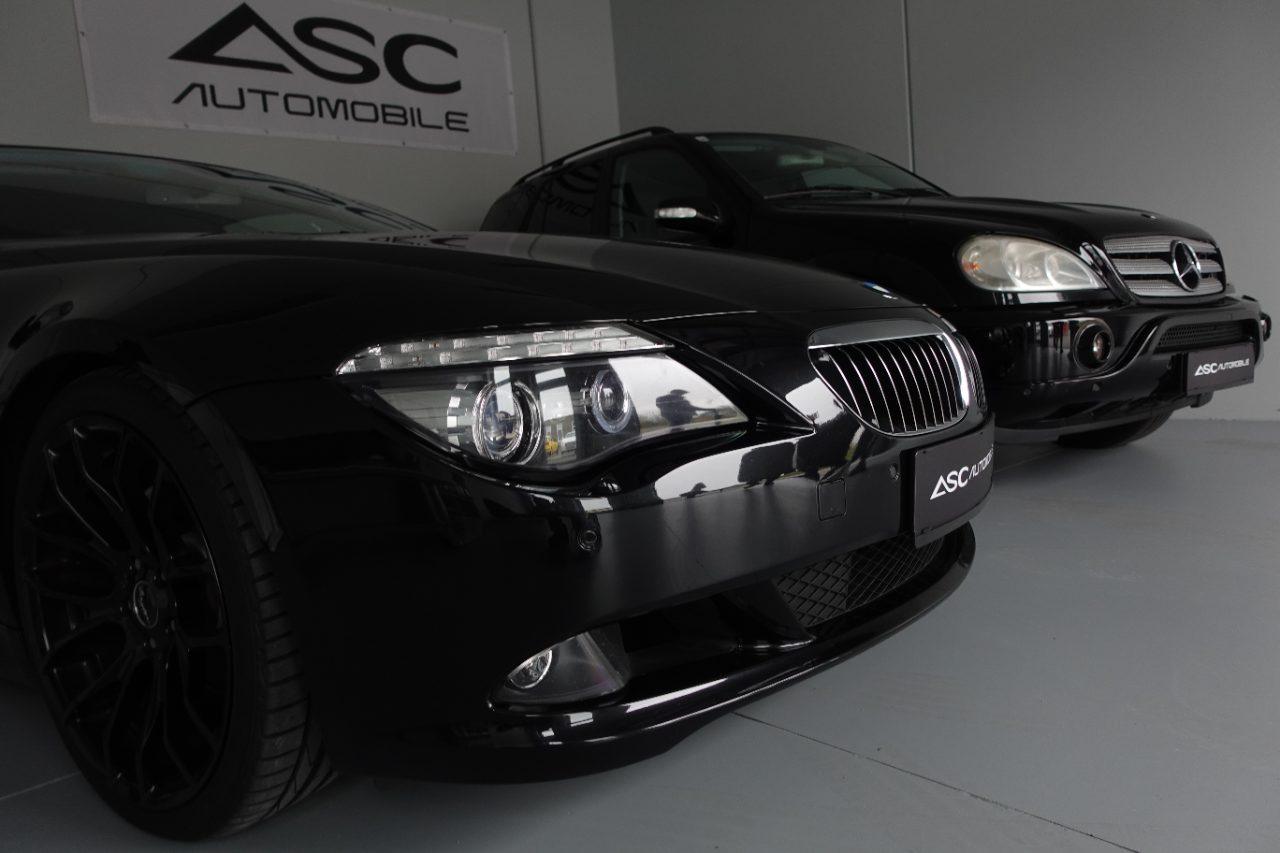 Nahaufnahme der Front eines schwarzen BMW Coupés im Showroom, dahinter ein schwarzer Mercedes SUV