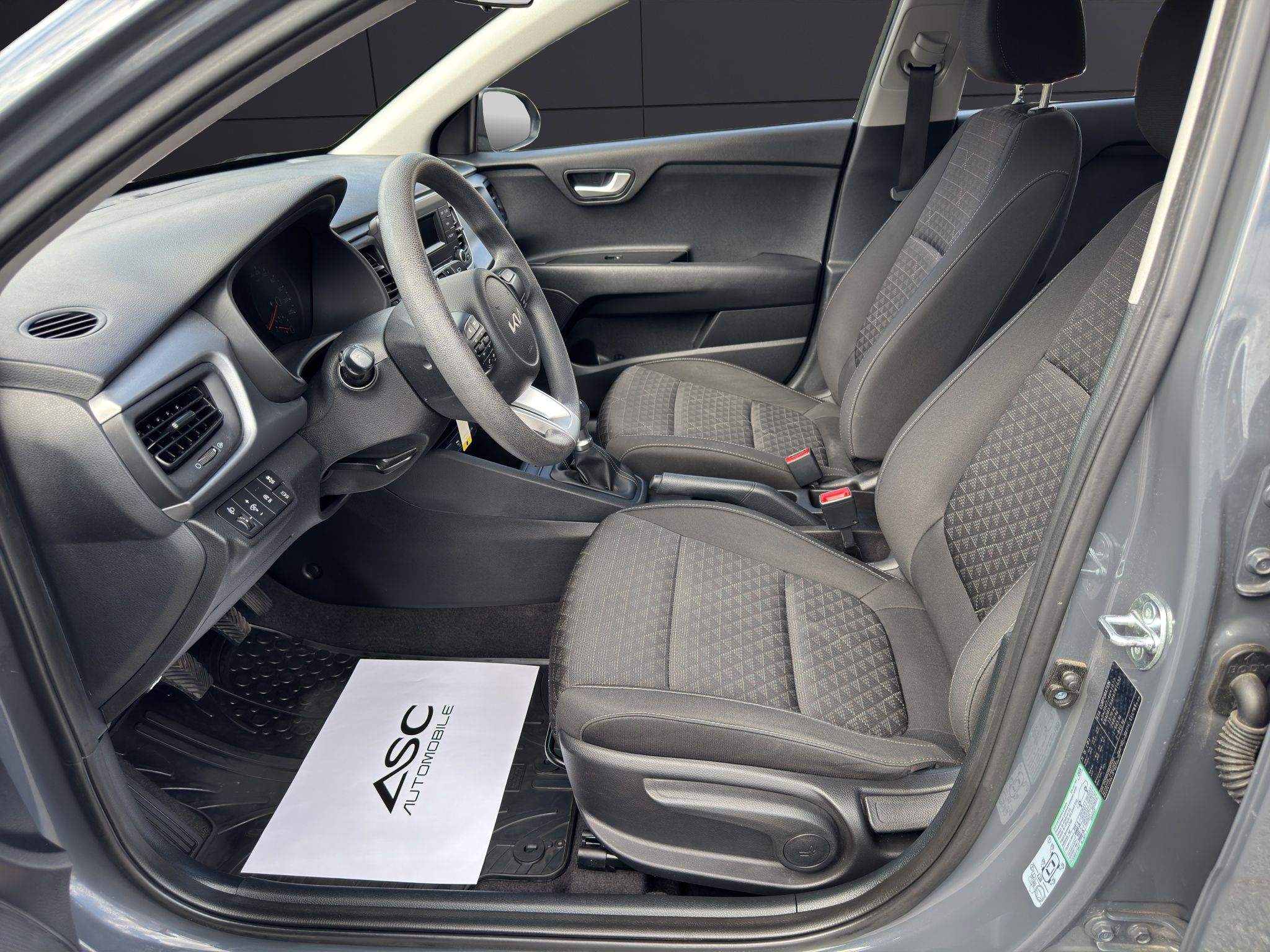 Blick durch die offene Fahrertür auf die Stoffsitze, den Schaltknauf und die Handbremse des KIA Rio