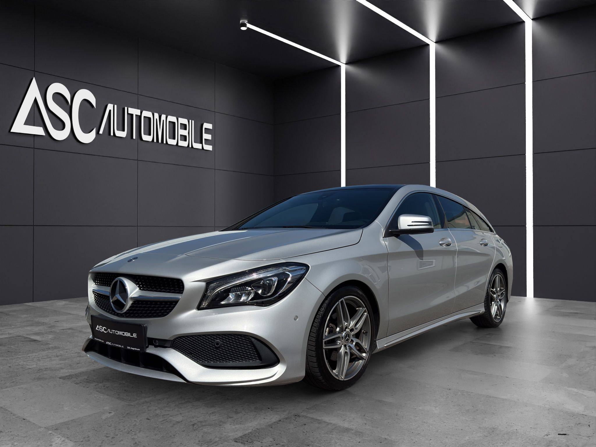 Mercedes-Benz CLA 180 Shooting Brake in Silber, schräg von vorne links im Showroom, mit AMG Line-Stoßfänger