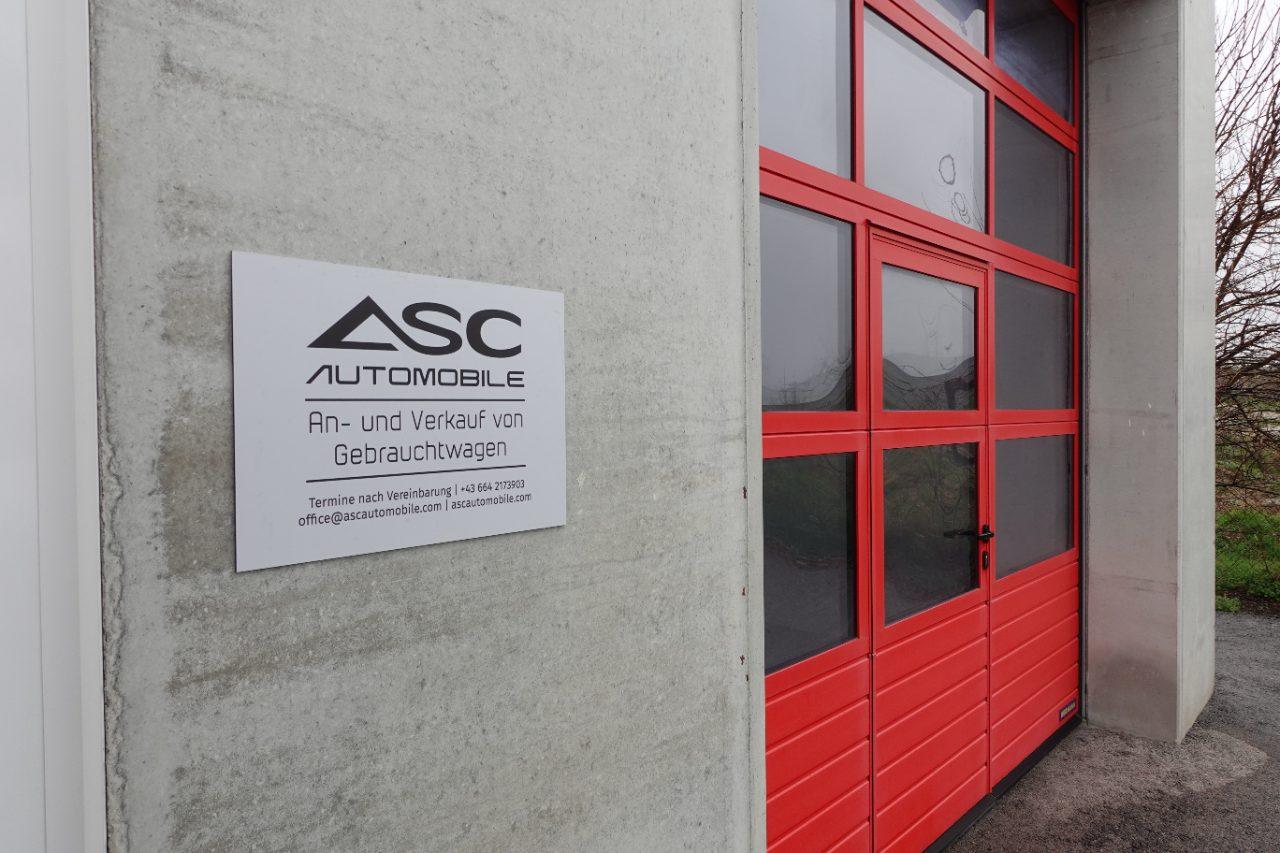 Firmenschild an der Halle: ASC Automobile, An- und Verkauf von Gebrauchtwagen, daneben ein rotes Hallentor