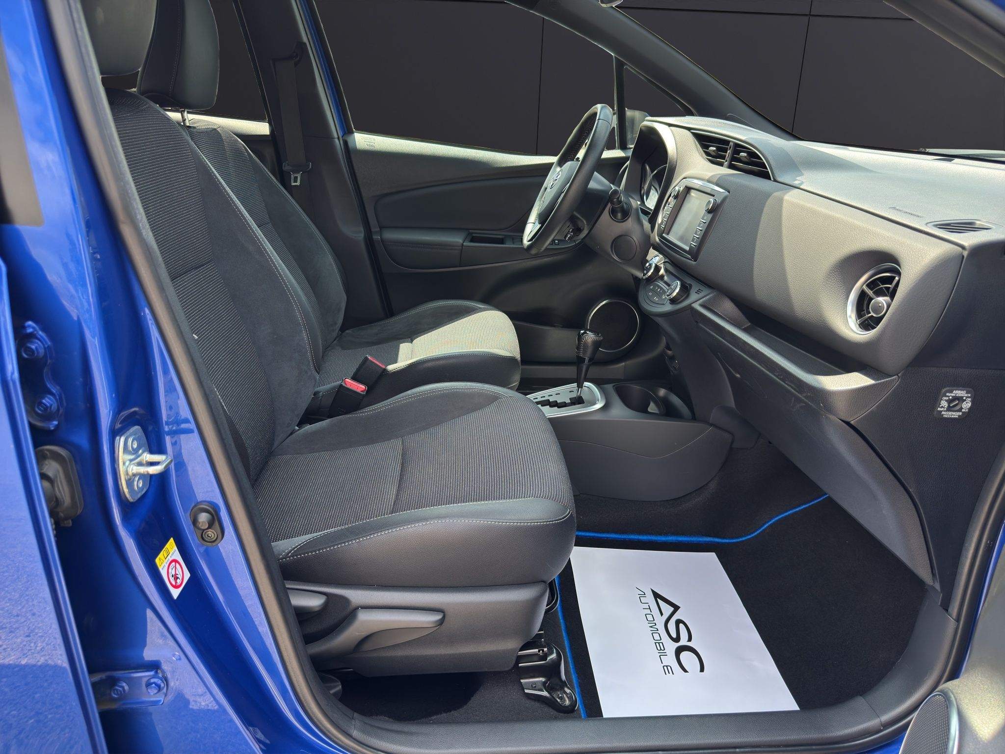 Vordersitze des Toyota Yaris in grauem Stoff, Blick durch die geöffnete Fahrertür